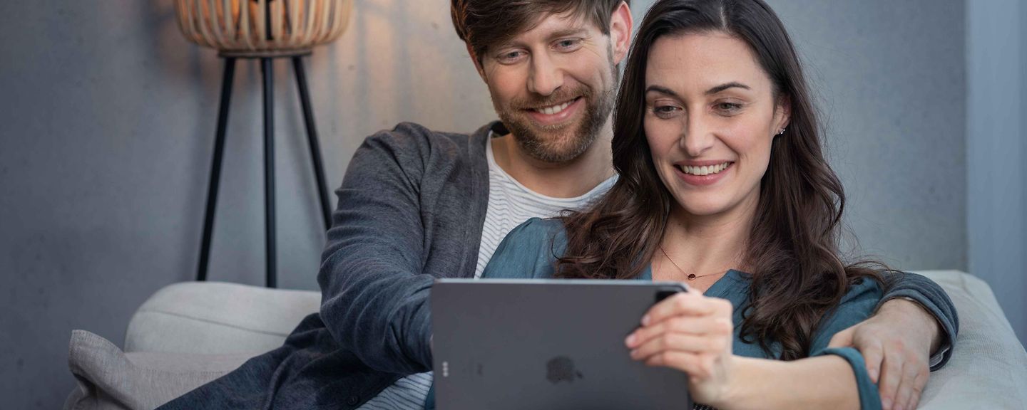 Paar sitzt mit Tablet auf der Couch