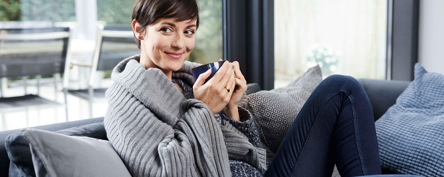 Frau sitzt mit einer Tasse auf der Couch